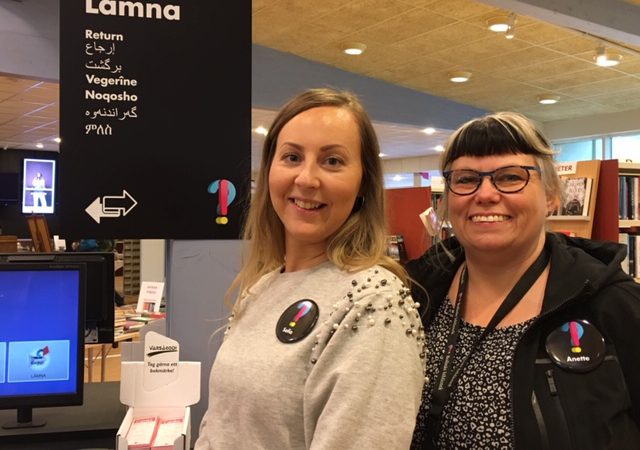 Bibliotekarierna Sofia Eliasson och Anette Helgesson på Bollnäs bibliote, framför en skylt sär det står "lämna" på svenska och sju andra språk.
