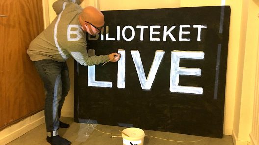 En man målar en skylt med texten "bibliotek live".